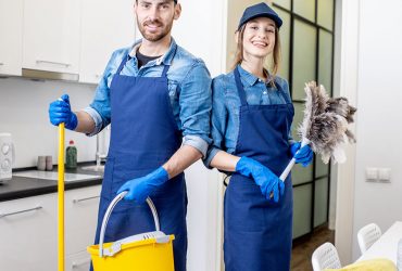 Portrait of a couple as a professional cleaners in uniform standing together with cleaning tools indoors